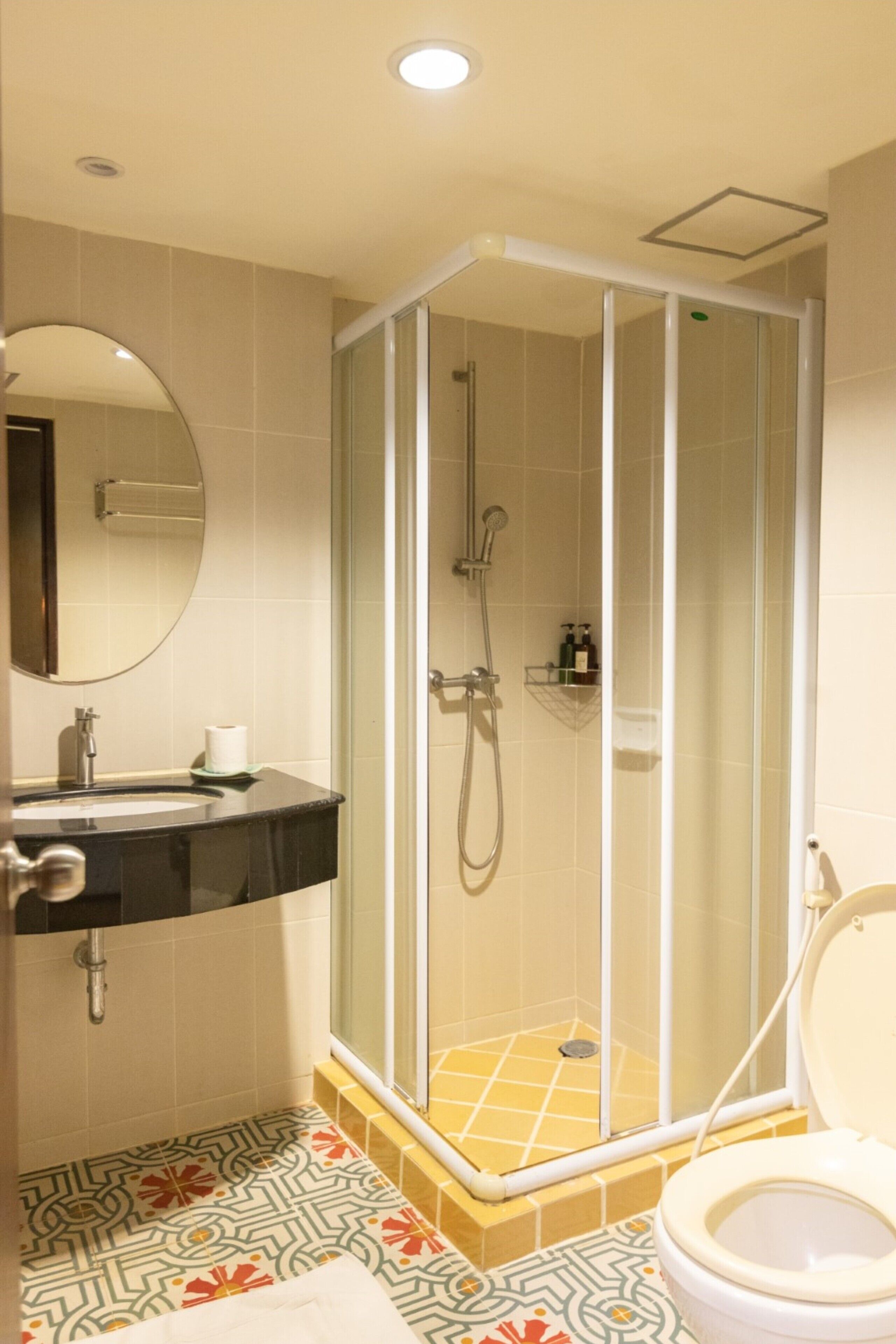 Un baño con ducha de vidrio, lavamanos con espejo e inodoro.