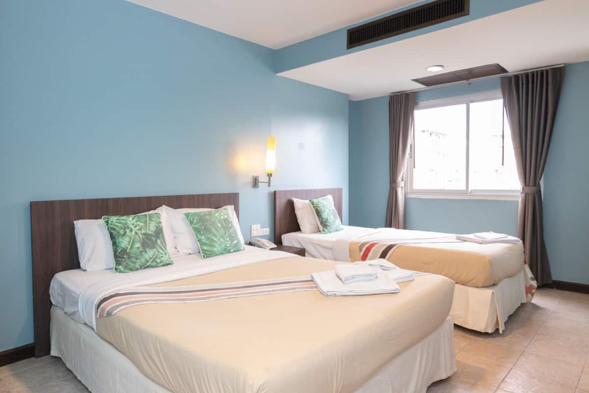 A hotel room with two beds, a window with curtains, a wall-mounted light, and a vent.