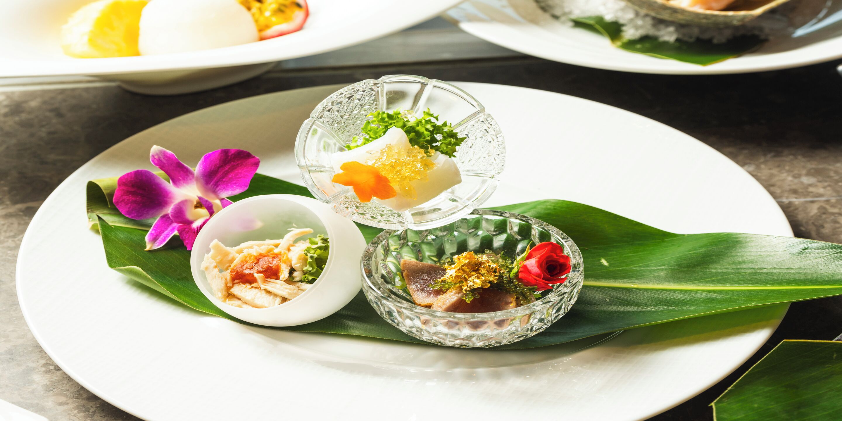 Un plato con tres recipientes de vidrio que contienen comida, una orquídea púrpura y una rosa roja.