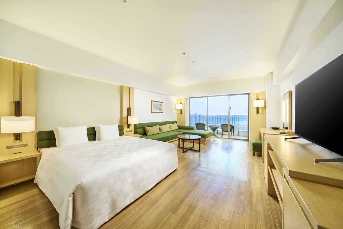 Une chambre d’hôtel avec un grand lit, un canapé, une télévision et un balcon donnant sur la mer.