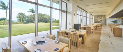A spacious dining area with large windows offering a view of a well-manicured lawn and palm trees.