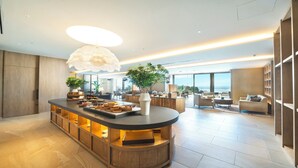 A modern hotel lobby with a central bar area, seating arrangements, and large windows offering a view of the sea.