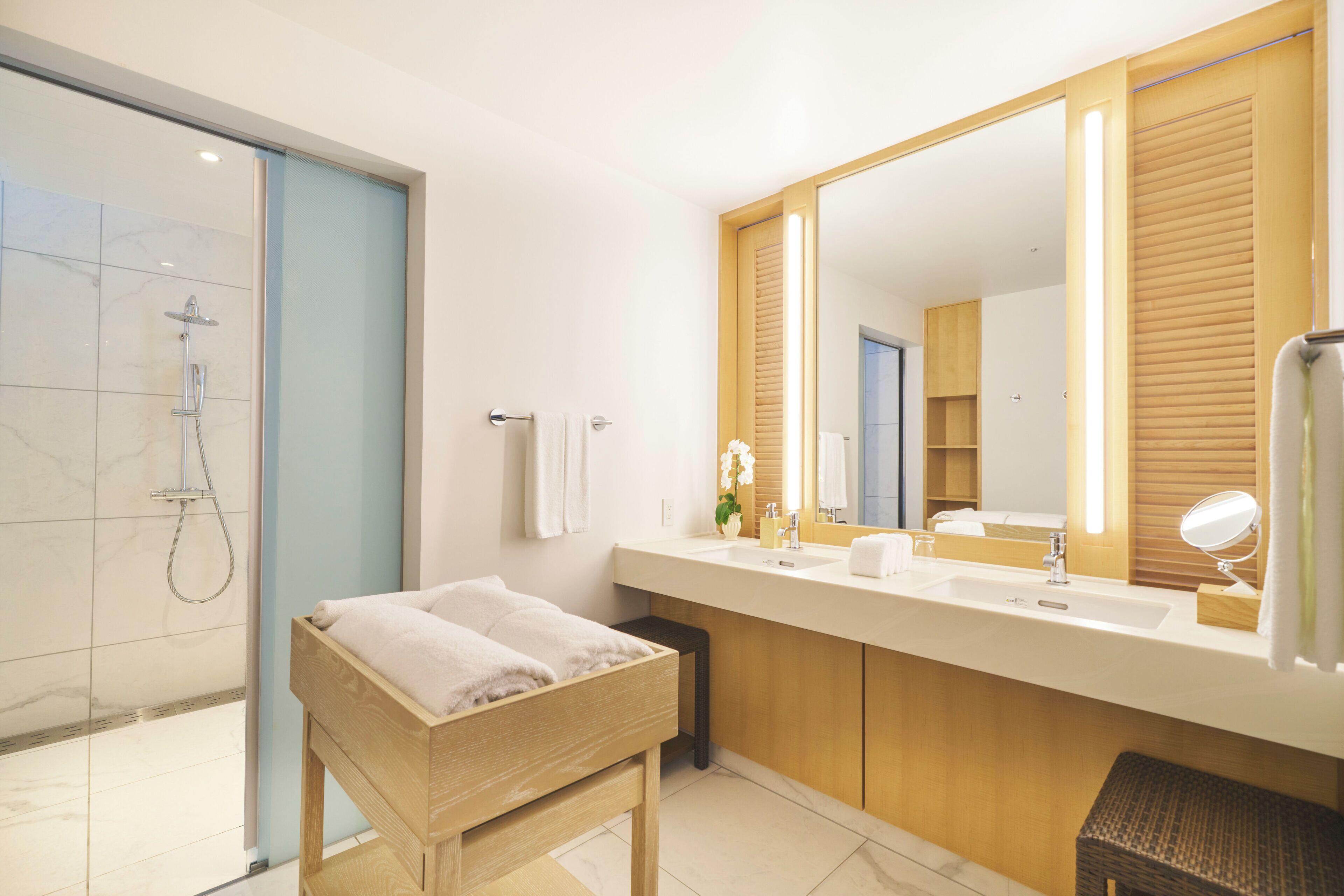 Un baño moderno con ducha, un banco de madera, un espejo grande y un tocador con lavamanos y perchero.
