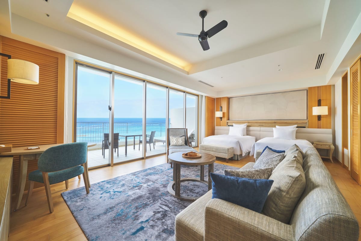 Une chambre d’hôtel moderne dotée d’un grand balcon, d’un lit, d’un canapé, d’un bureau et d’une chaise.