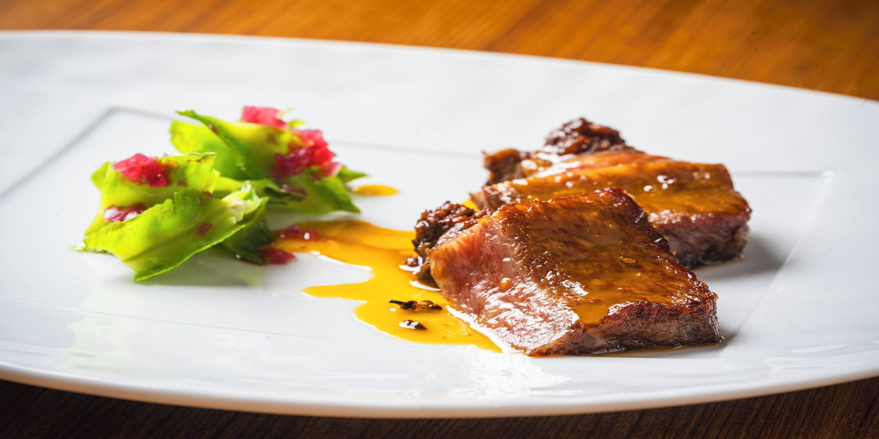 A plate with two pieces of meat and a green salad with red accents.