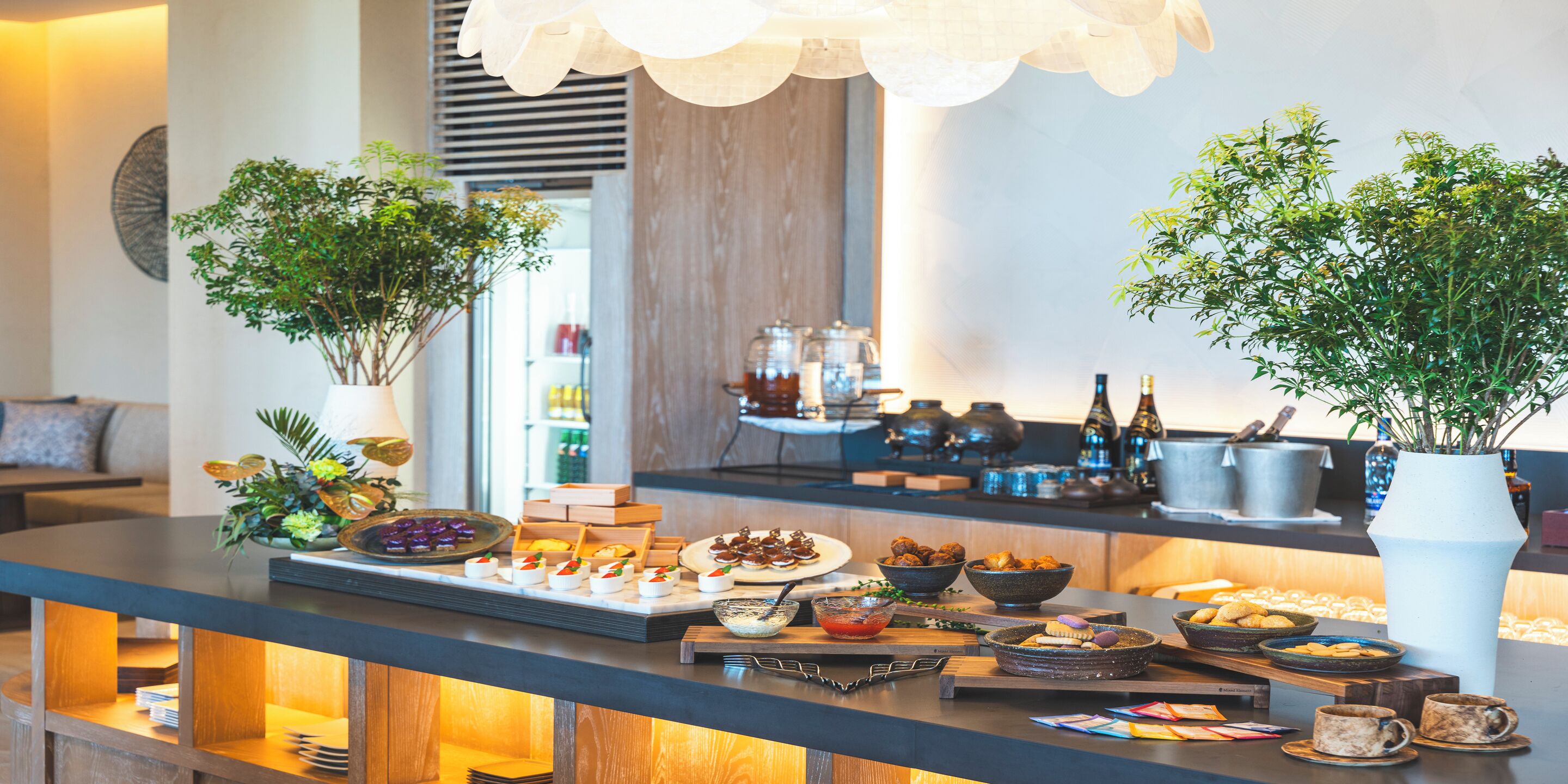 A buffet setup with various food items and decorative plants.