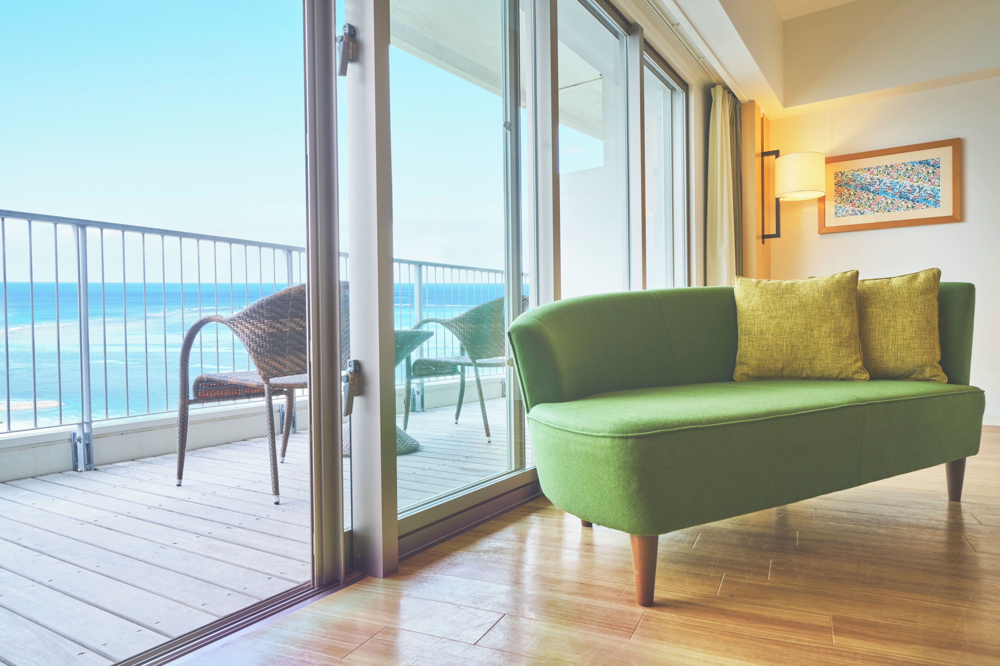A green sofa with two cushions, a wicker chair, and a wooden floor.