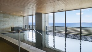 A large indoor swimming pool with a view of the sea through large windows.
