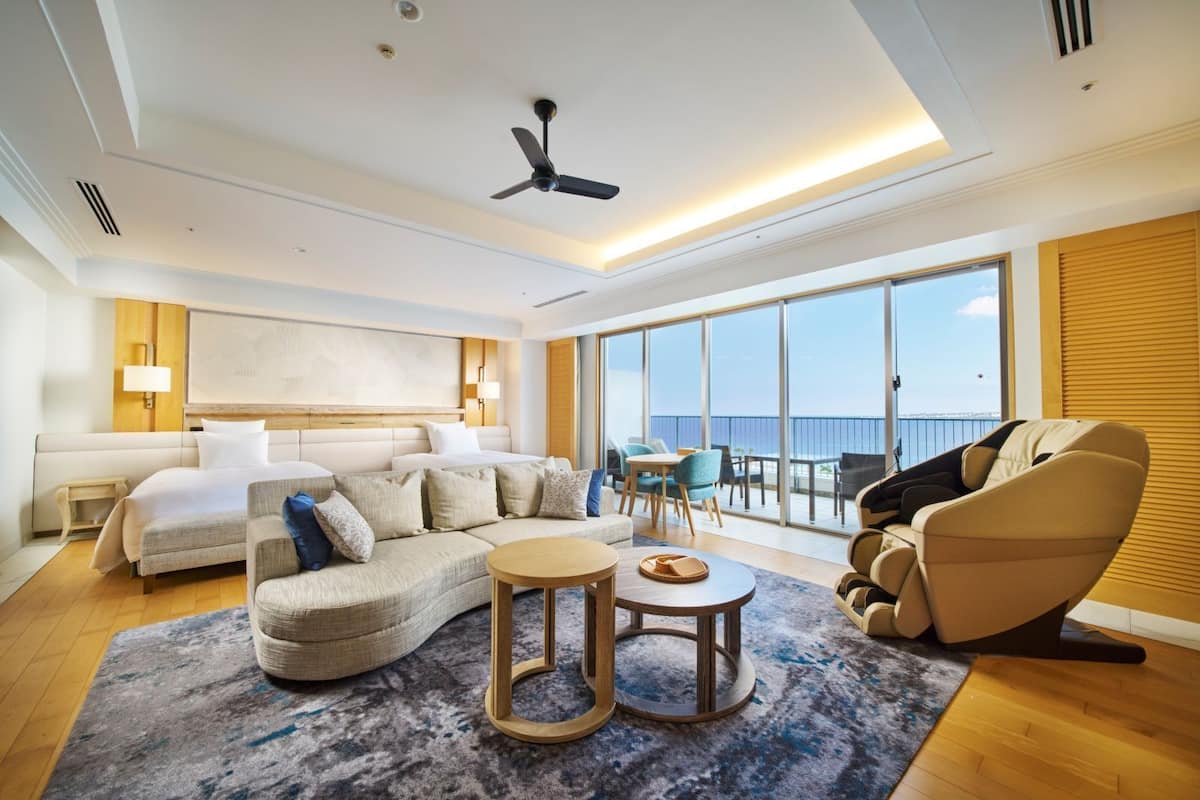 Une chambre d’hôtel moderne dotée d’un grand lit, d’un canapé, d’un fauteuil, d’une petite table et offrant une vue sur la mer.