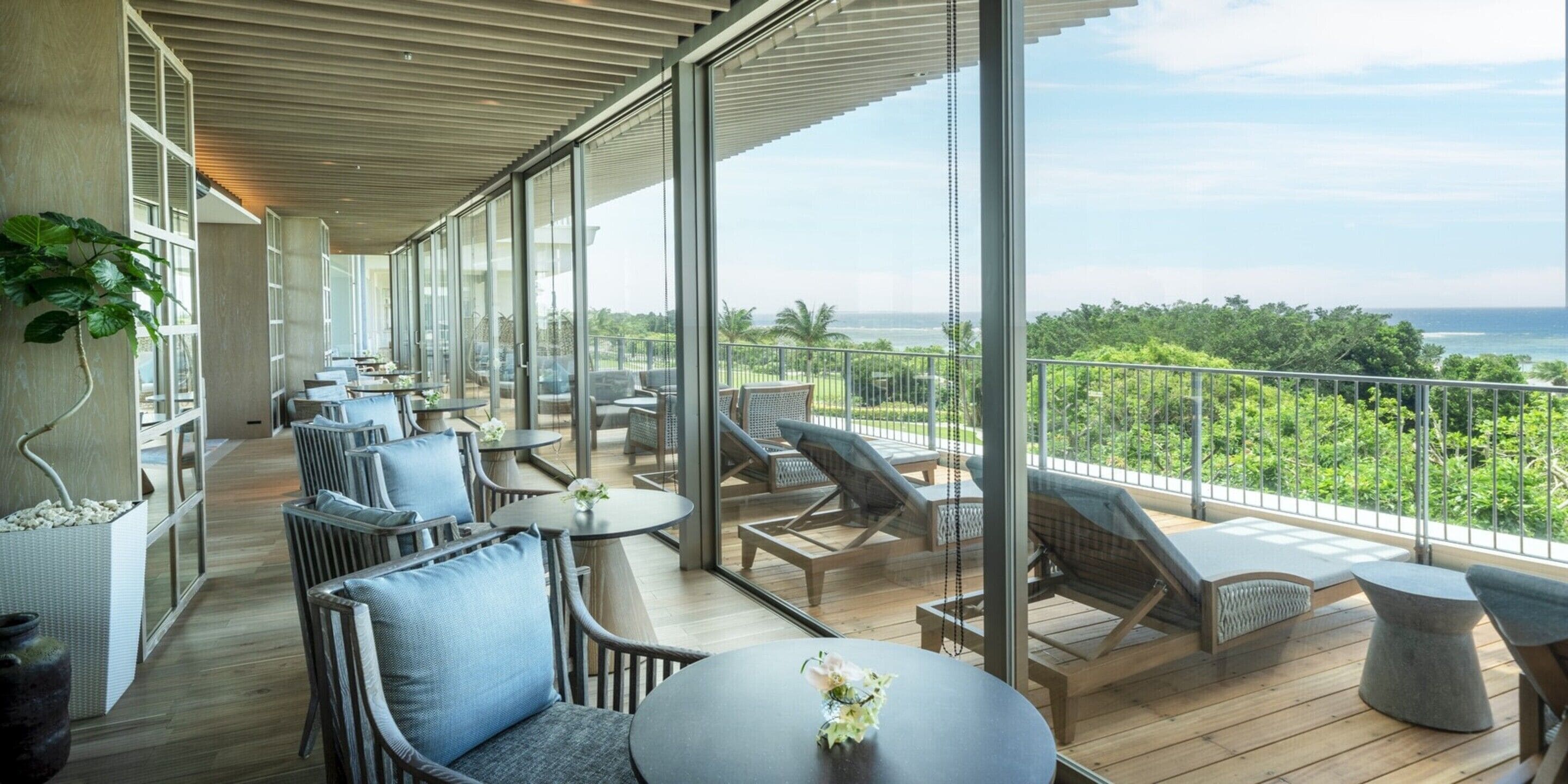 A spacious balcony with modern furniture, large windows, and a view of the ocean.