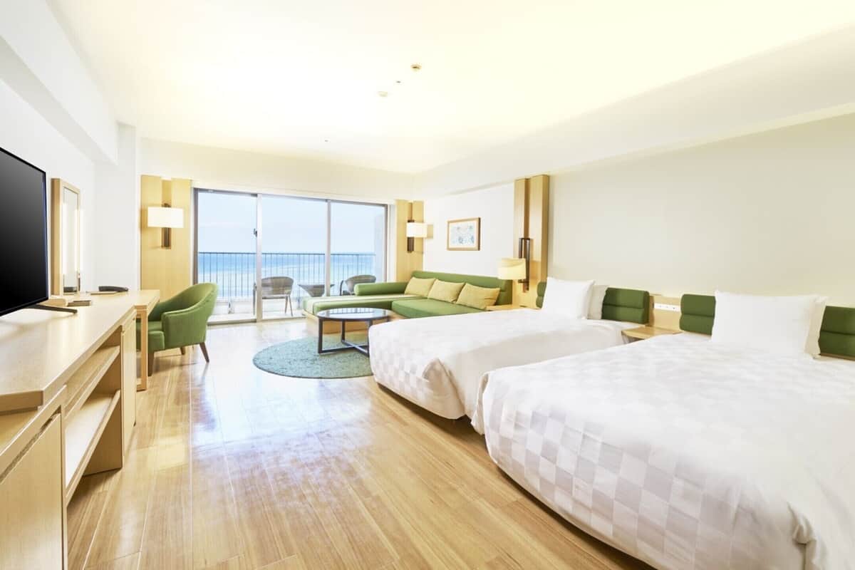 Une chambre d’hôtel avec un grand lit, un lit plus petit, un bureau, une télévision et un balcon avec vue.