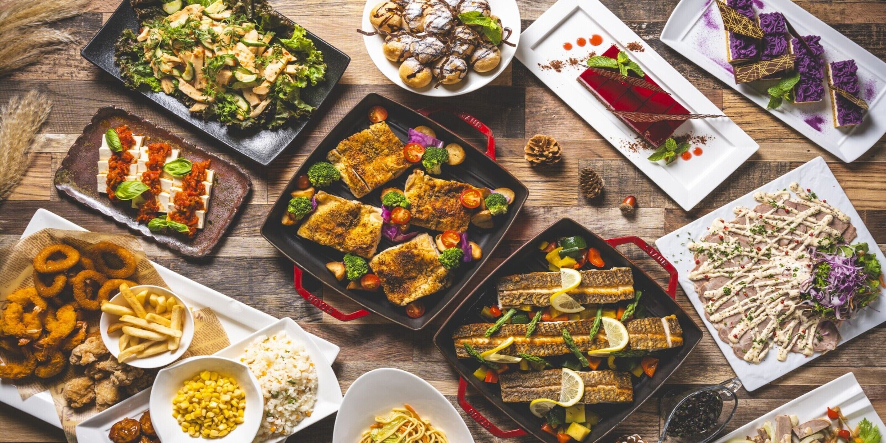 A variety of dishes including grilled fish, salads, and desserts on a wooden table.