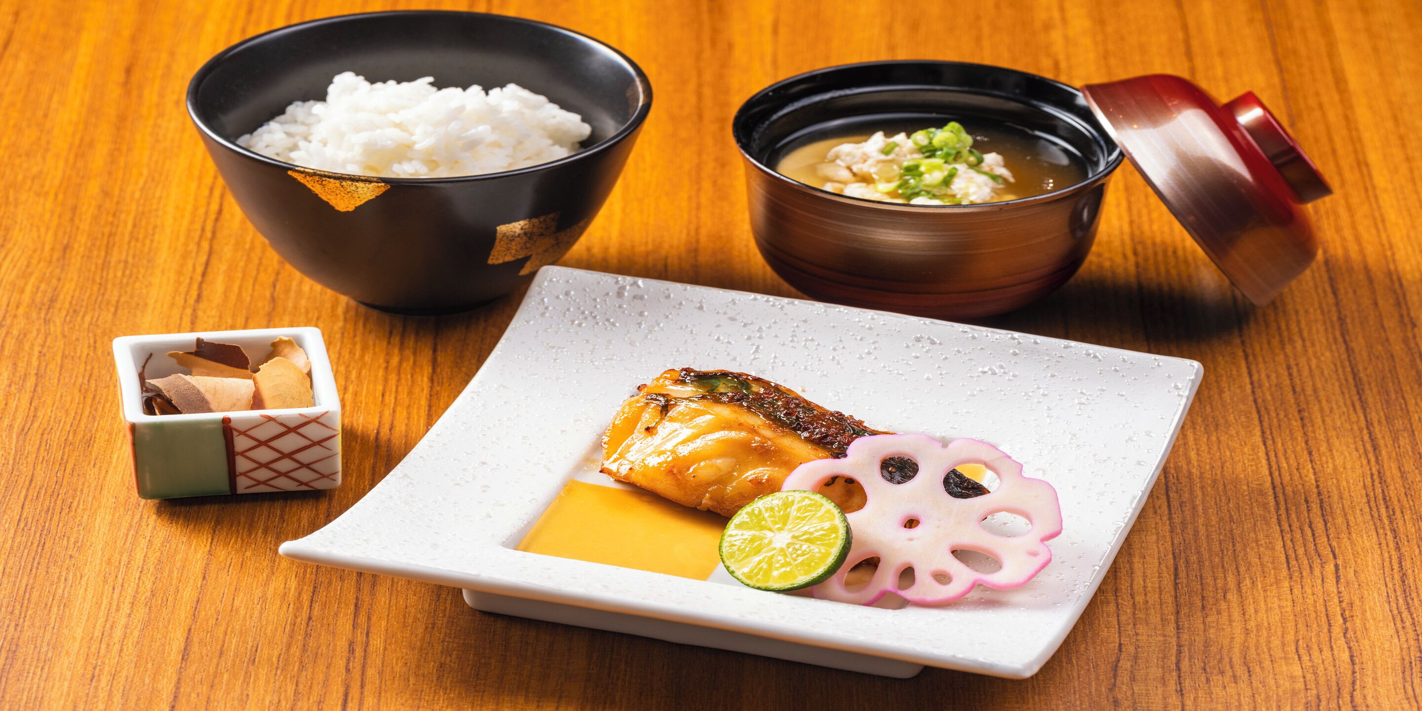 A traditional Japanese meal with rice, soup, grilled fish, and pickled vegetables on a wooden table.