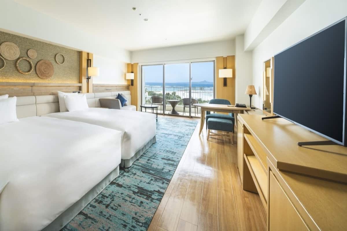 Une chambre d’hôtel avec deux lits, un bureau, une télévision et un balcon avec vue.