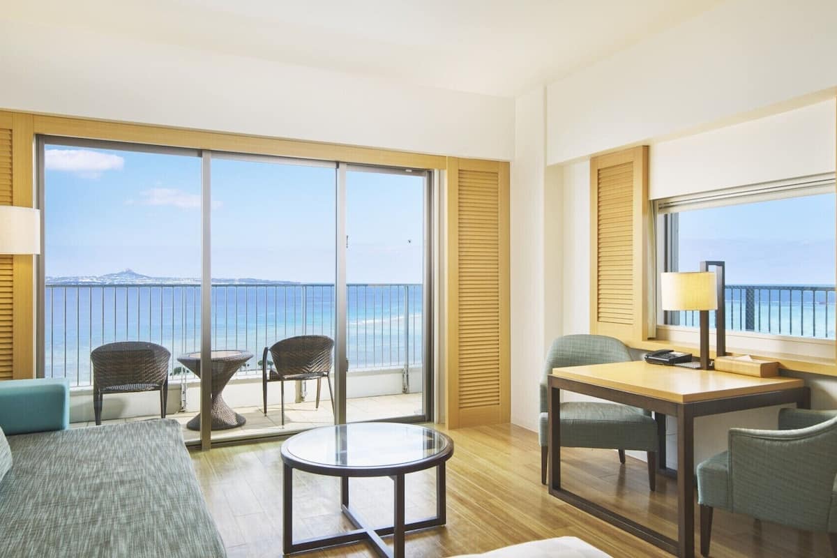 Une chambre d’hôtel avec un balcon, une table ronde, deux chaises, un canapé et une lampe.