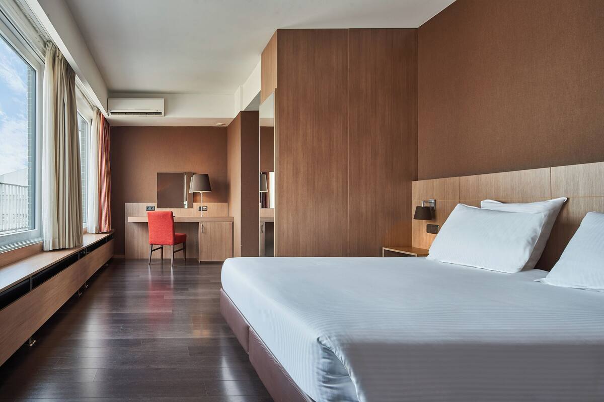 A modern hotel room with a large bed, a desk, and a chair.