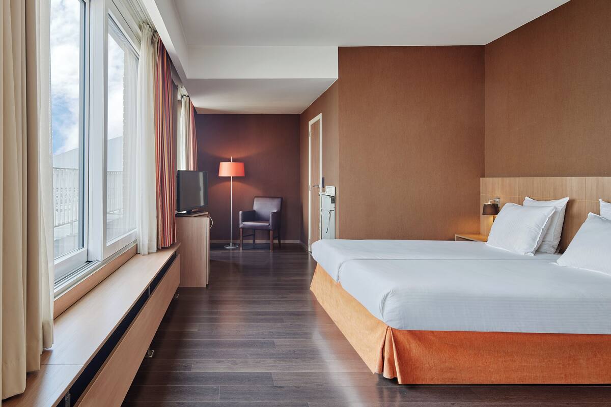 A hotel room with a large bed, a TV, a desk, and a chair.