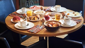 A breakfast table with plates of eggs, bacon, toast, and fruit. There are cups of coffee and juice, and a bowl of croissants. - Theater Hotel (Antwerp)