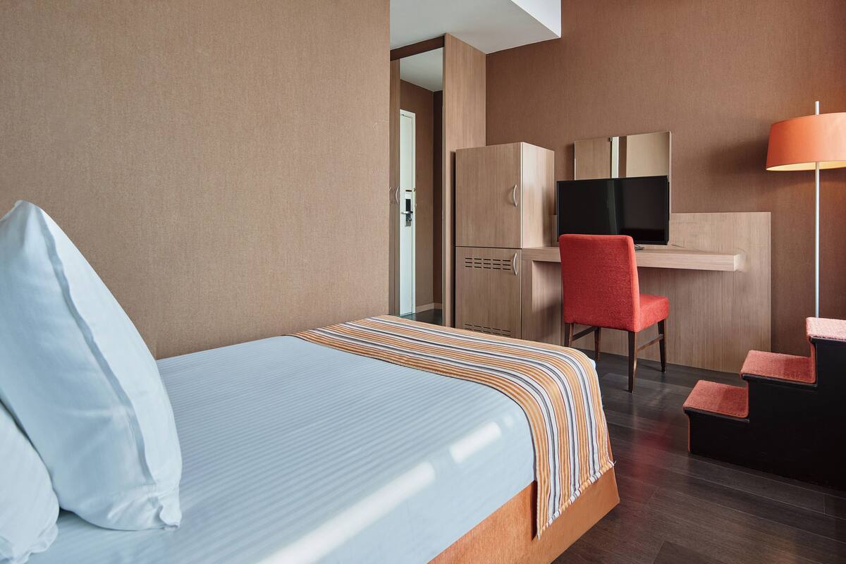A hotel room with a bed, a desk with a chair, a television, and a lamp.