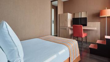 A hotel room with a bed, a desk with a chair, a television, and a lamp.
