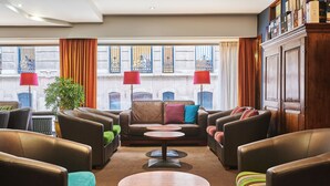 A modern lounge with leather sofas, a central coffee table, and a large window with curtains. - Theater Hotel (Antwerp)