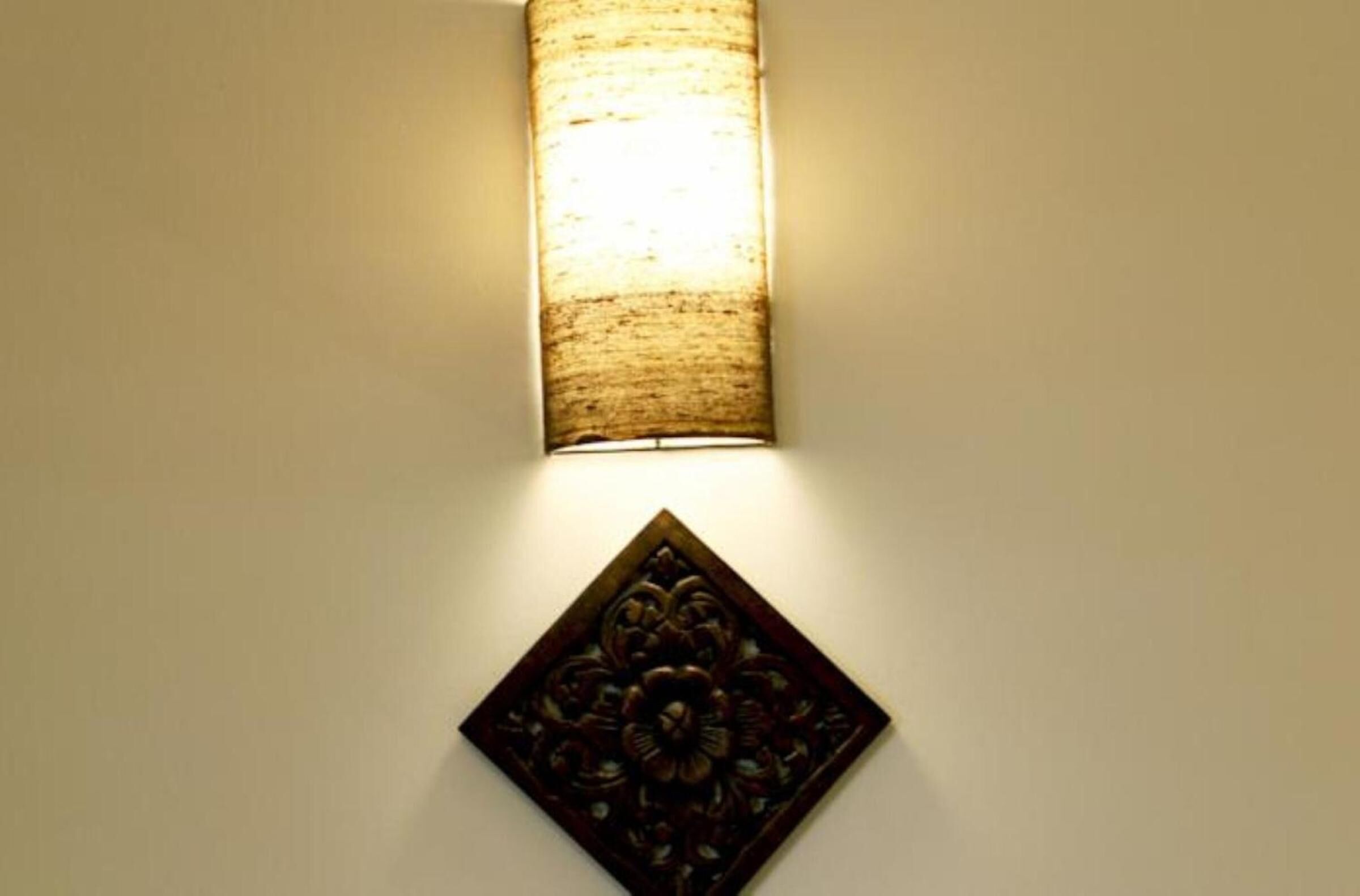A wall-mounted light fixture with a textured shade and a decorative panel below it.