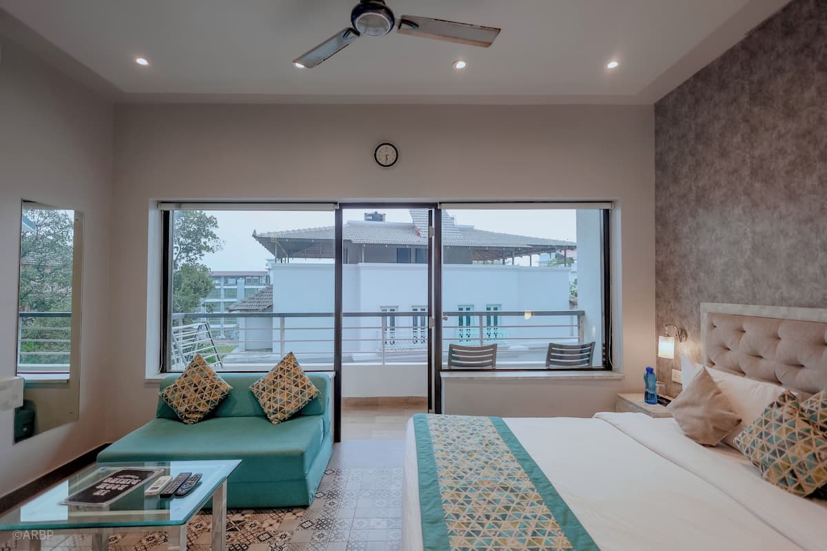 Una habitación de hotel moderna con un balcón grande, una cama con ropa de cama estampada, un sofá con cojines geométricos y una mesa de centro de vidrio.