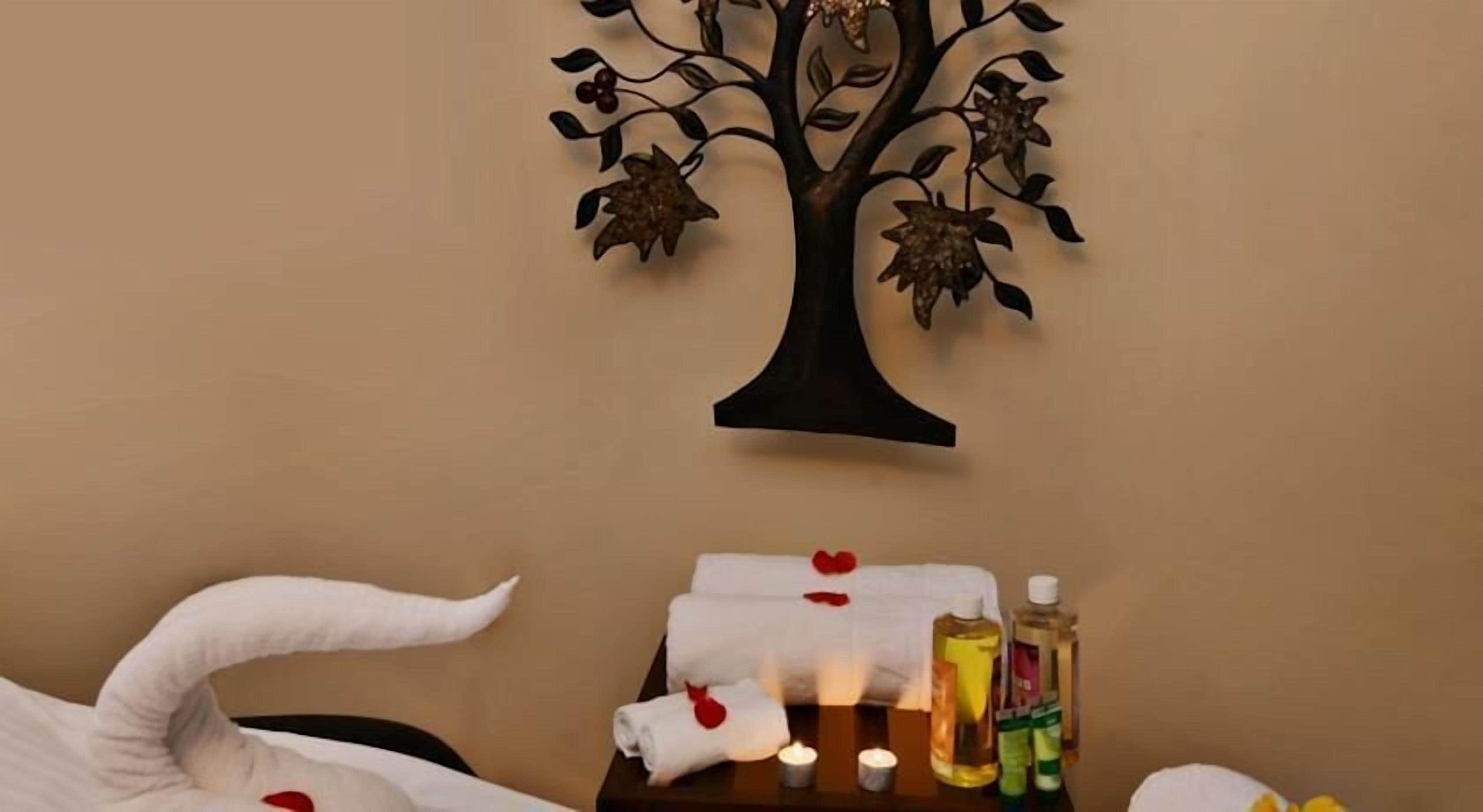 Ein Spa-Raum mit einer an der Wand befestigten Baumdekoration, einem Handtuch mit einem roten Herz, Kerzen und Pflegeprodukten auf einem Tisch.