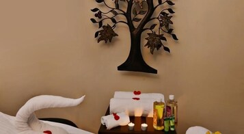 Ein Spa-Raum mit einer an der Wand befestigten Baumdekoration, einem Handtuch mit einem roten Herz, Kerzen und Pflegeprodukten auf einem Tisch.