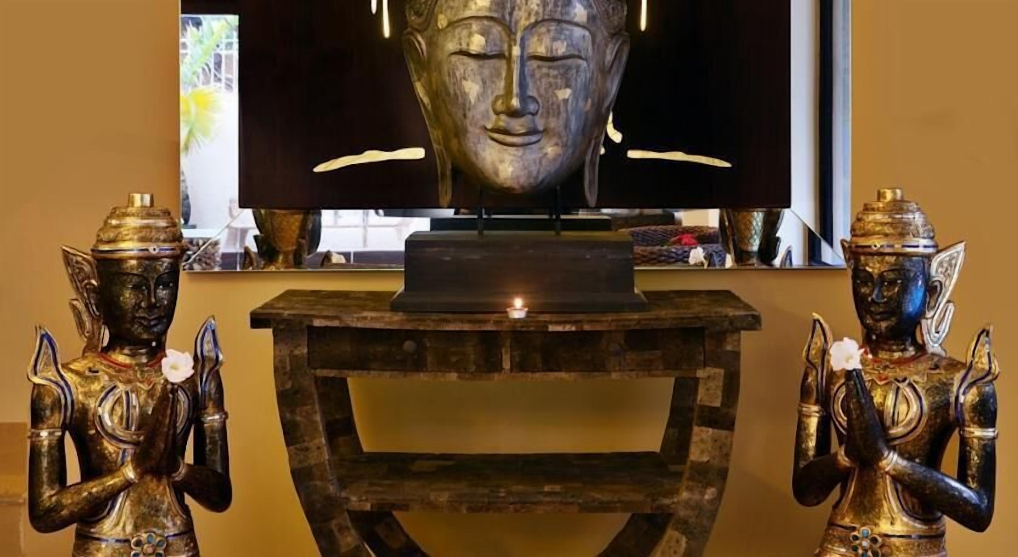 Una habitación con un televisor sobre una mesa de madera, flanqueada por dos estatuas doradas.