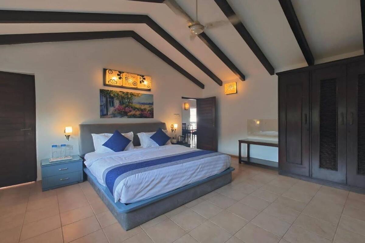 Un dormitorio con una cama grande, una mesita de noche, un cuadro sobre la cama y un ventilador de techo.