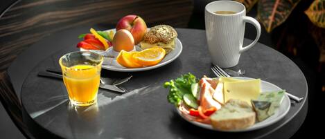 Una mesa redonda con un plato de frutas, verduras, queso y un muffin, acompañado de un vaso de jugo de naranja y una taza de café.