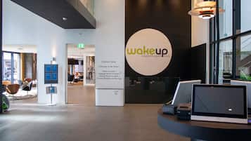 Un moderno vestíbulo de hotel con una recepción, un gran logotipo circular y señales indicativas hacia servicios como el centro de negocios y los ascensores.