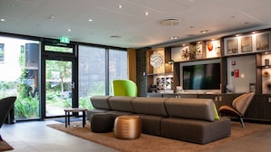 A modern lobby with a large sofa, green chair, and a flat-screen TV.