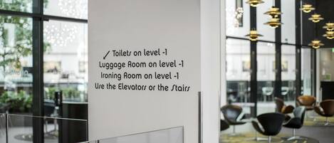 Un moderno vestíbulo de hotel con una pared de vidrio, un letrero blanco con indicaciones a los servicios y muebles contemporáneos.