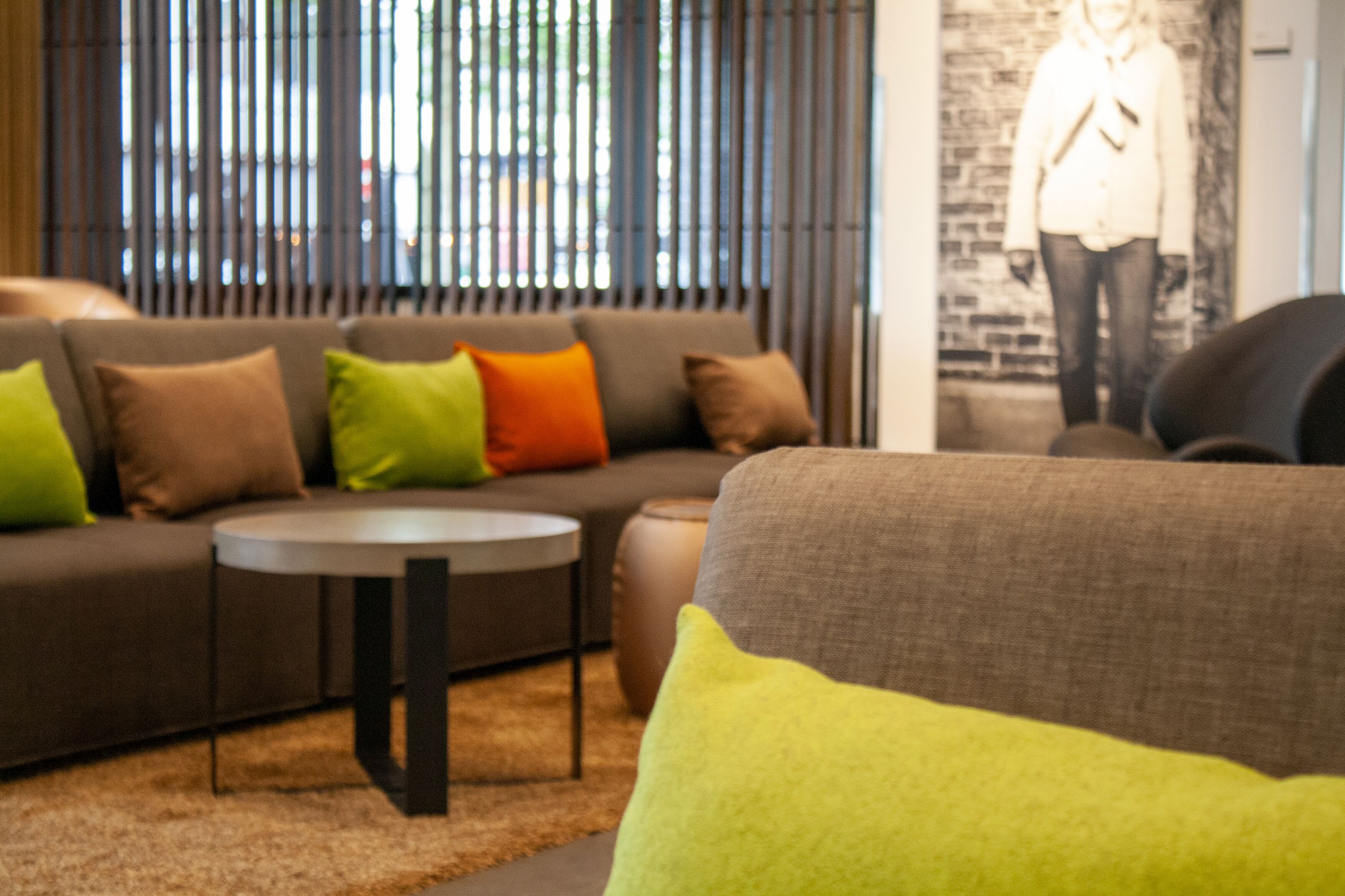 A modern living room with a sofa, a round coffee table, and a large window with vertical blinds.