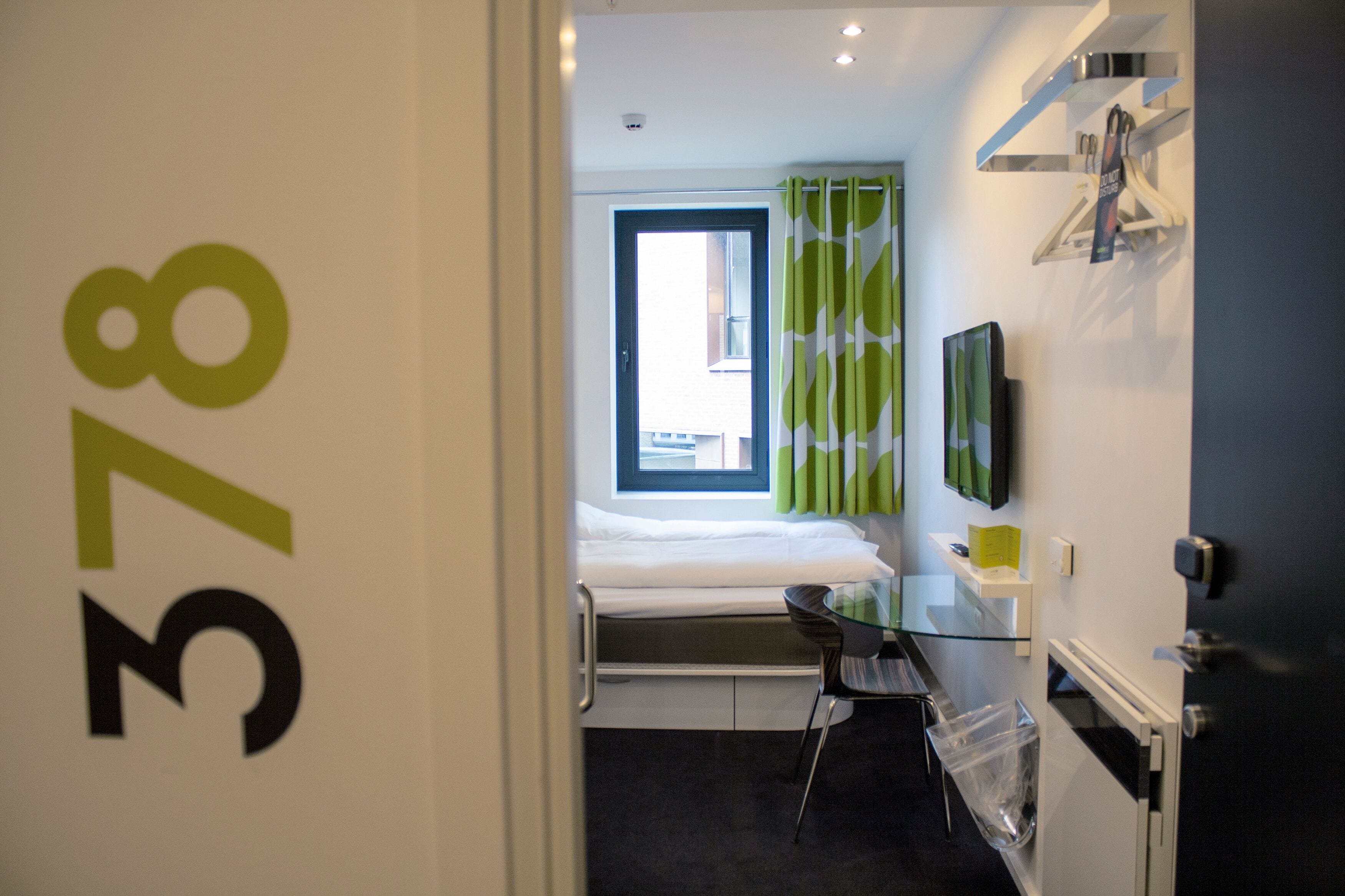 A hotel room with a bed, a desk, a chair, a TV, and a window with curtains.
