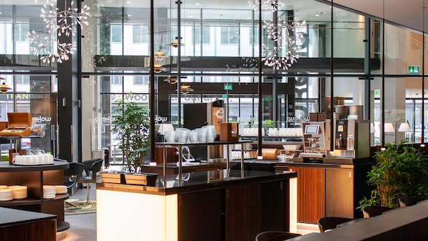 A modern bar area with a counter, seating, and a view of the street through large windows.
