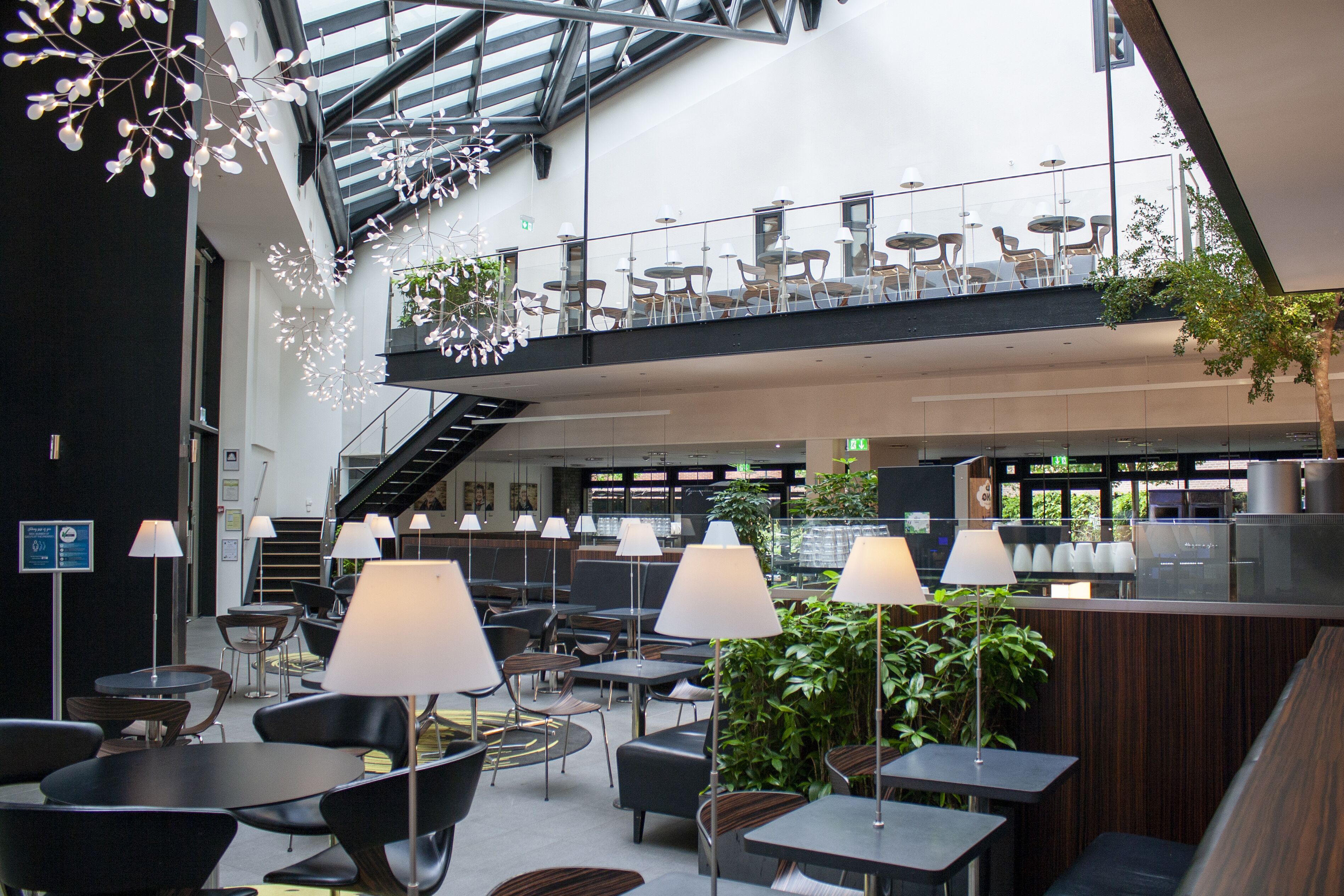 A spacious indoor area with multiple seating arrangements, including tables and chairs, and a staircase leading to an upper level.