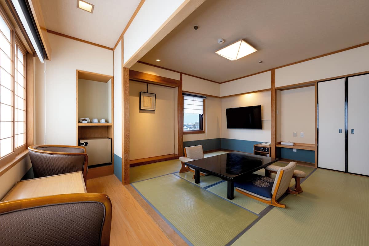 Une pièce de style japonais traditionnel, avec un sol recouvert de tatamis, une table basse, des sièges, un téléviseur et des portes coulissantes.