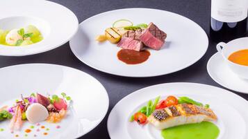 A table with four plates of food, a bottle of wine, and a cup of soup.