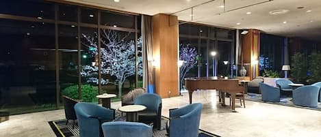 A hotel lobby with a piano, seating area, and large windows with a view of trees.