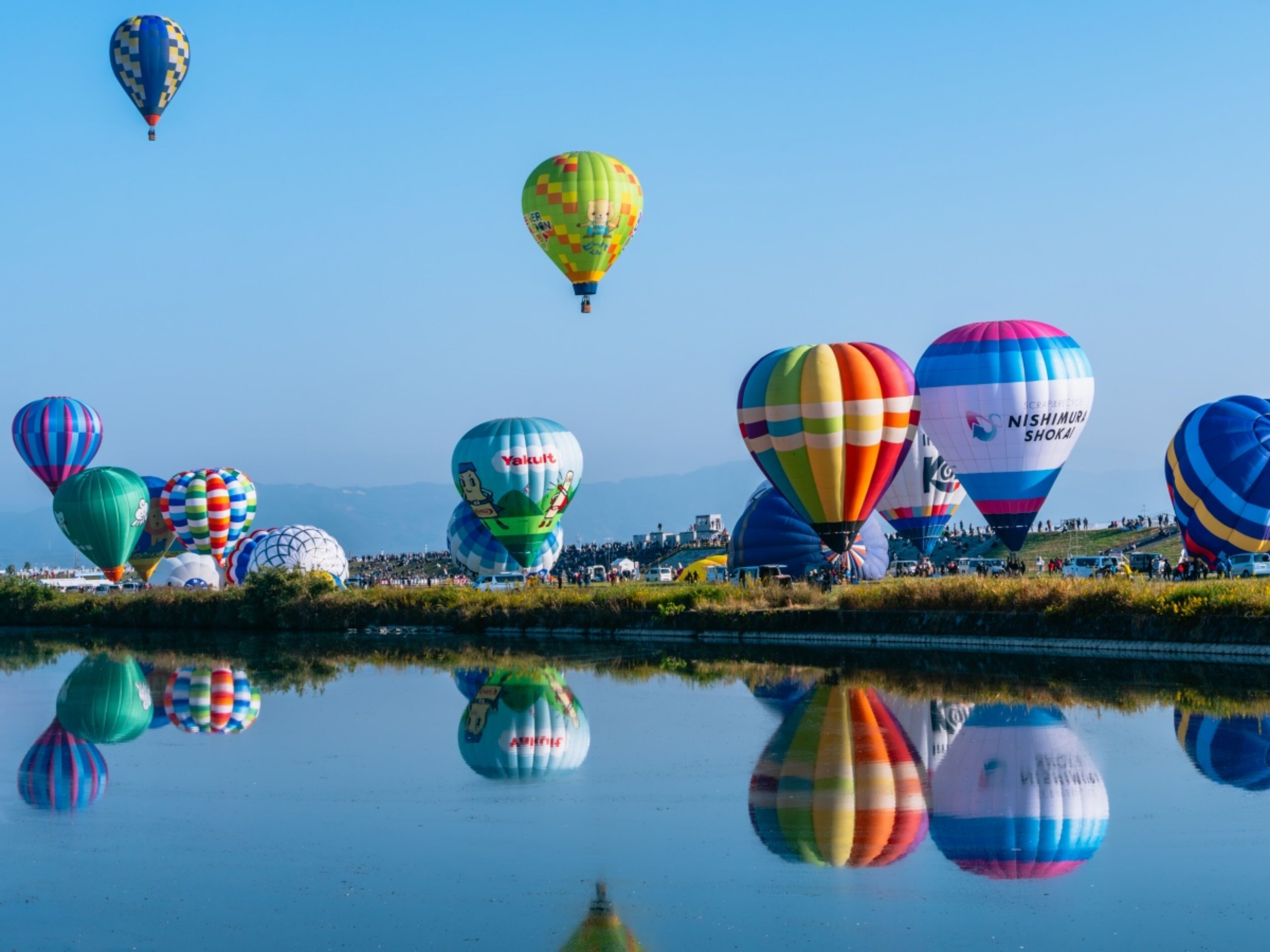 A variety of colorful hot air balloons over a body of water with reflections.