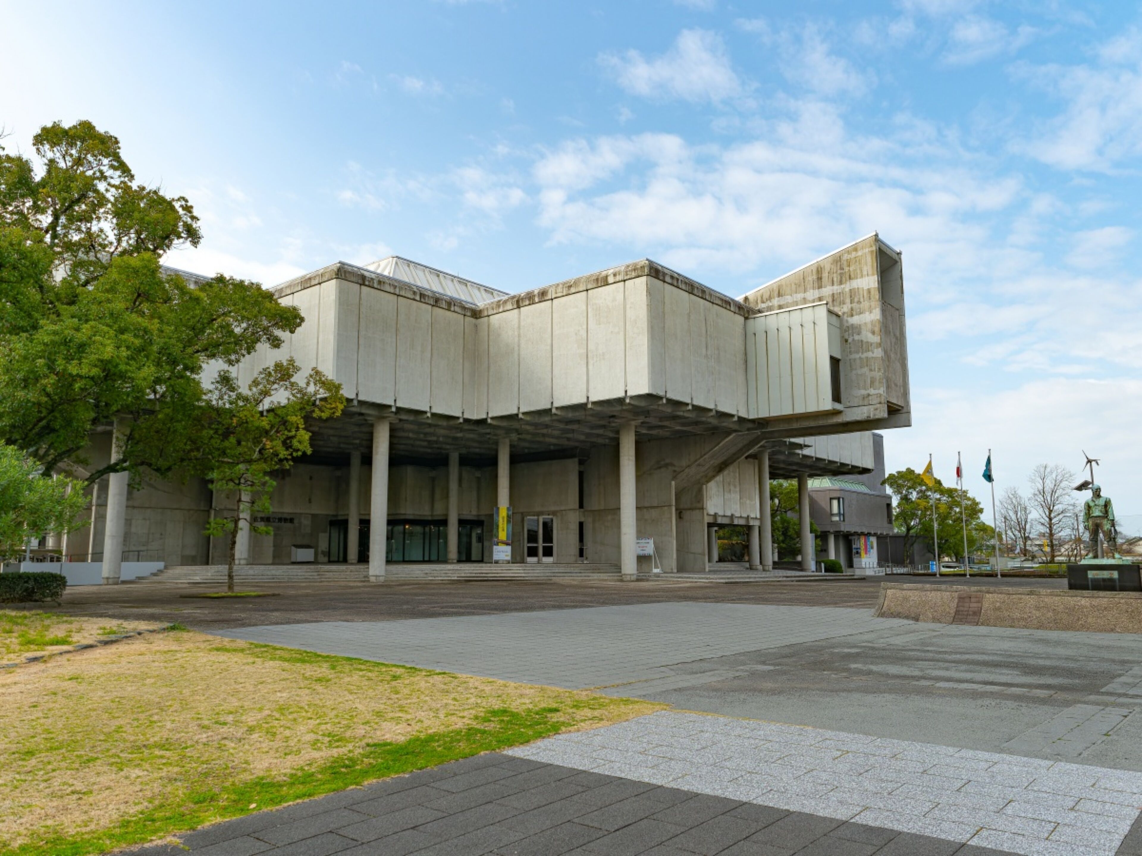 A modern building with a unique architectural design, featuring a large open plaza and a statue in the foreground.