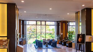 A spacious lobby with a polished marble floor, large windows offering a view of a garden, and a seating area with chairs and a table.