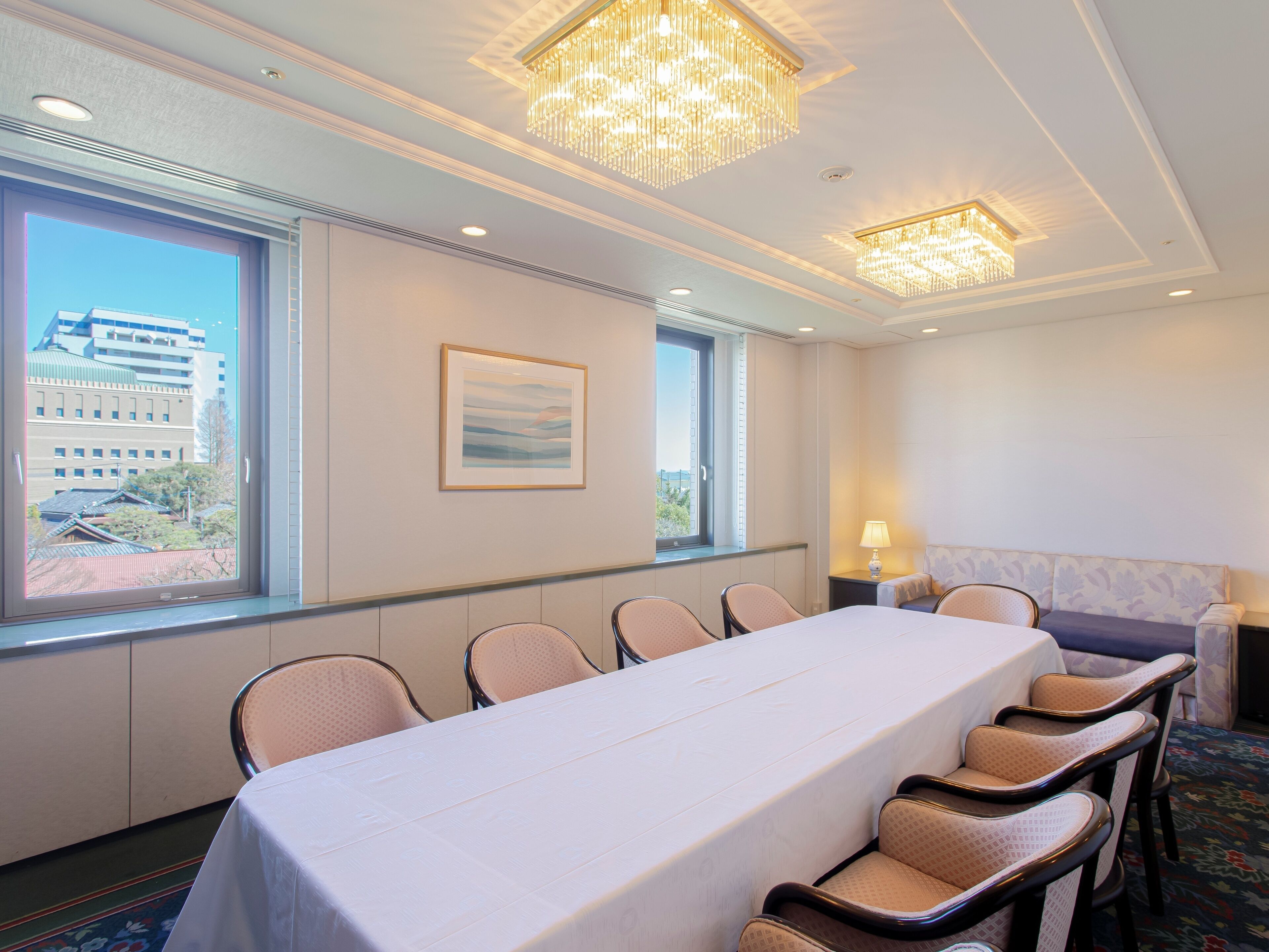 A conference room with a long table, chairs, a chandelier, and a window with a city view.