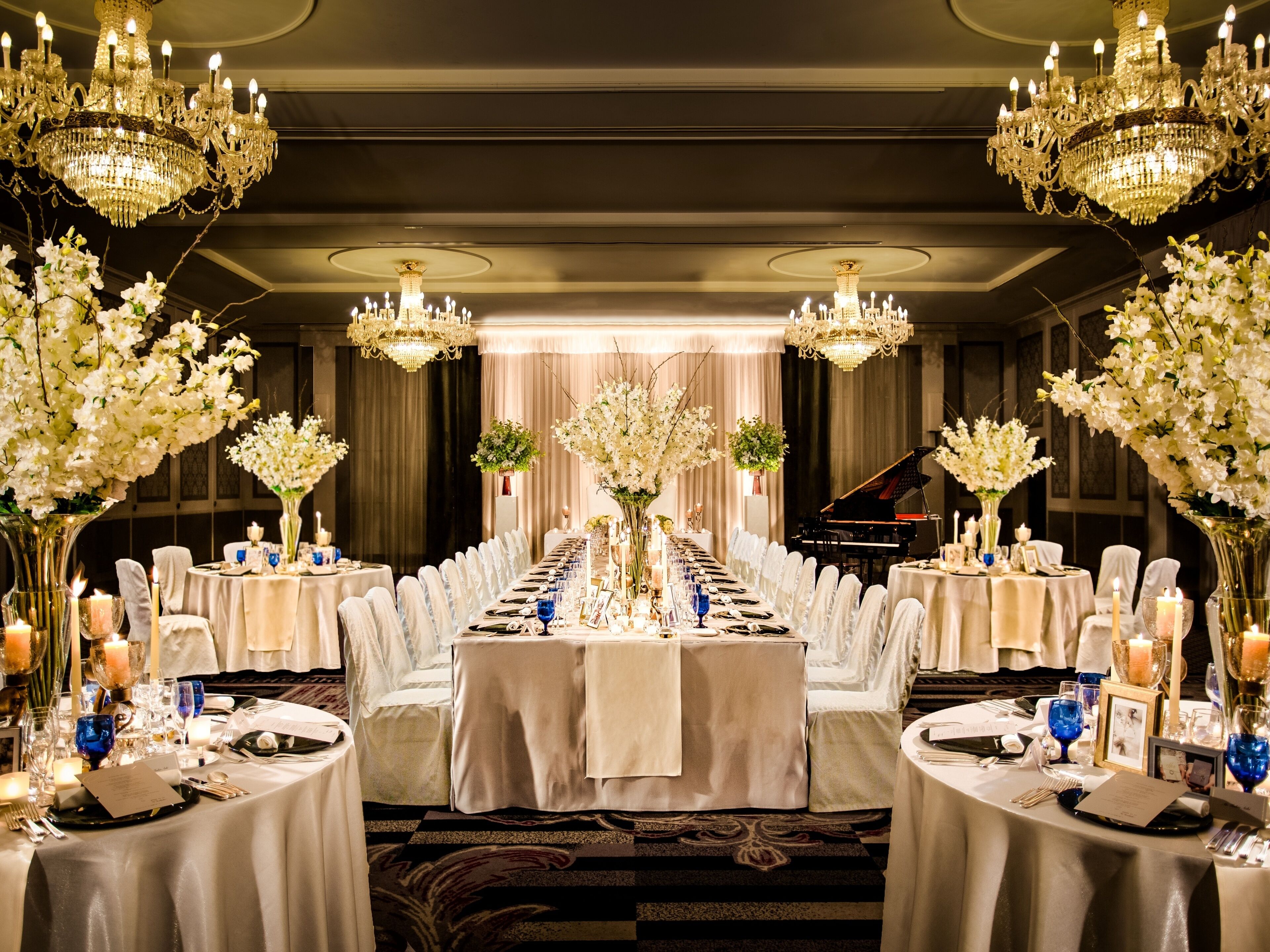 A banquet hall with long tables, chandeliers, and a grand piano.
