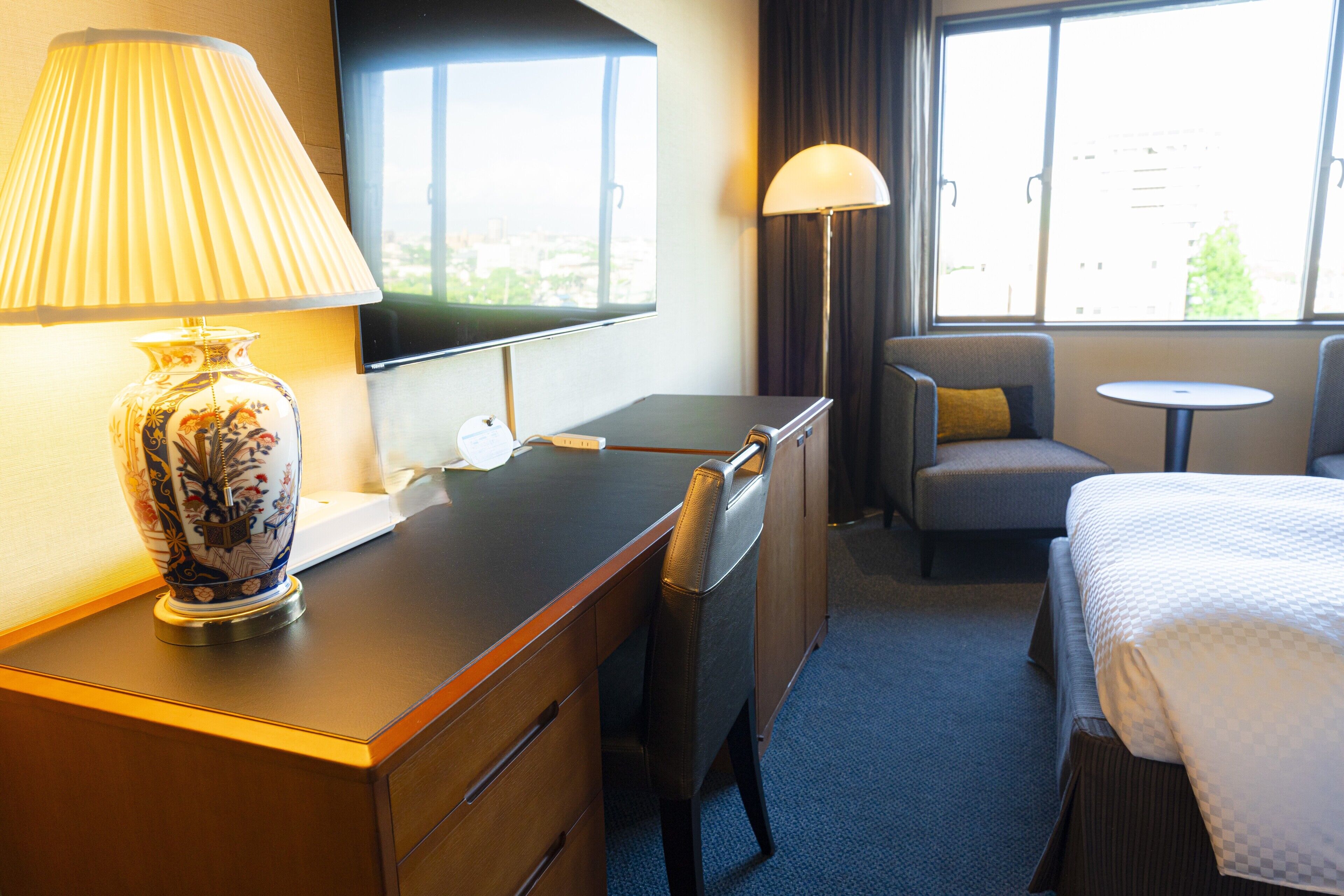A hotel room with a desk, a chair, a bed, a television, and a window with a view.