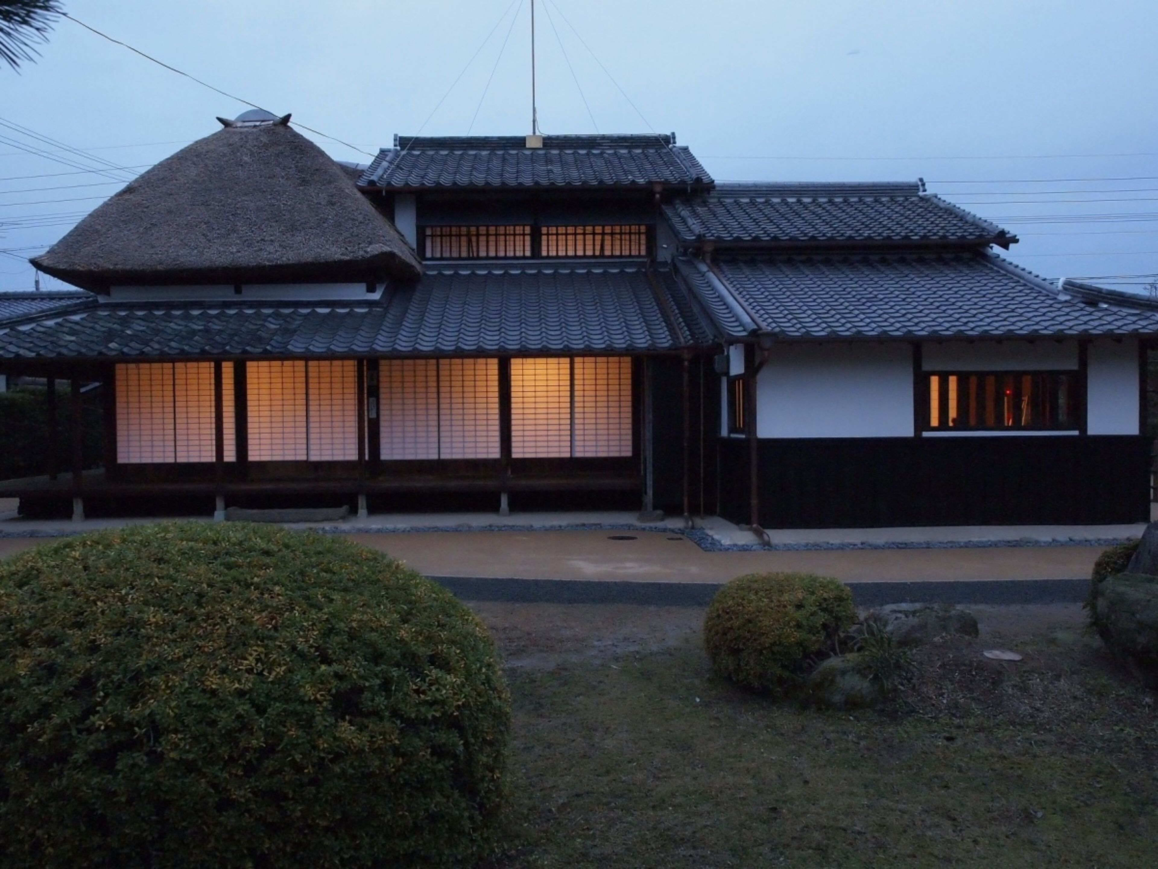 A traditional Japanese building with a thatched roof and wooden walls, featuring sliding doors and a tiled roof.