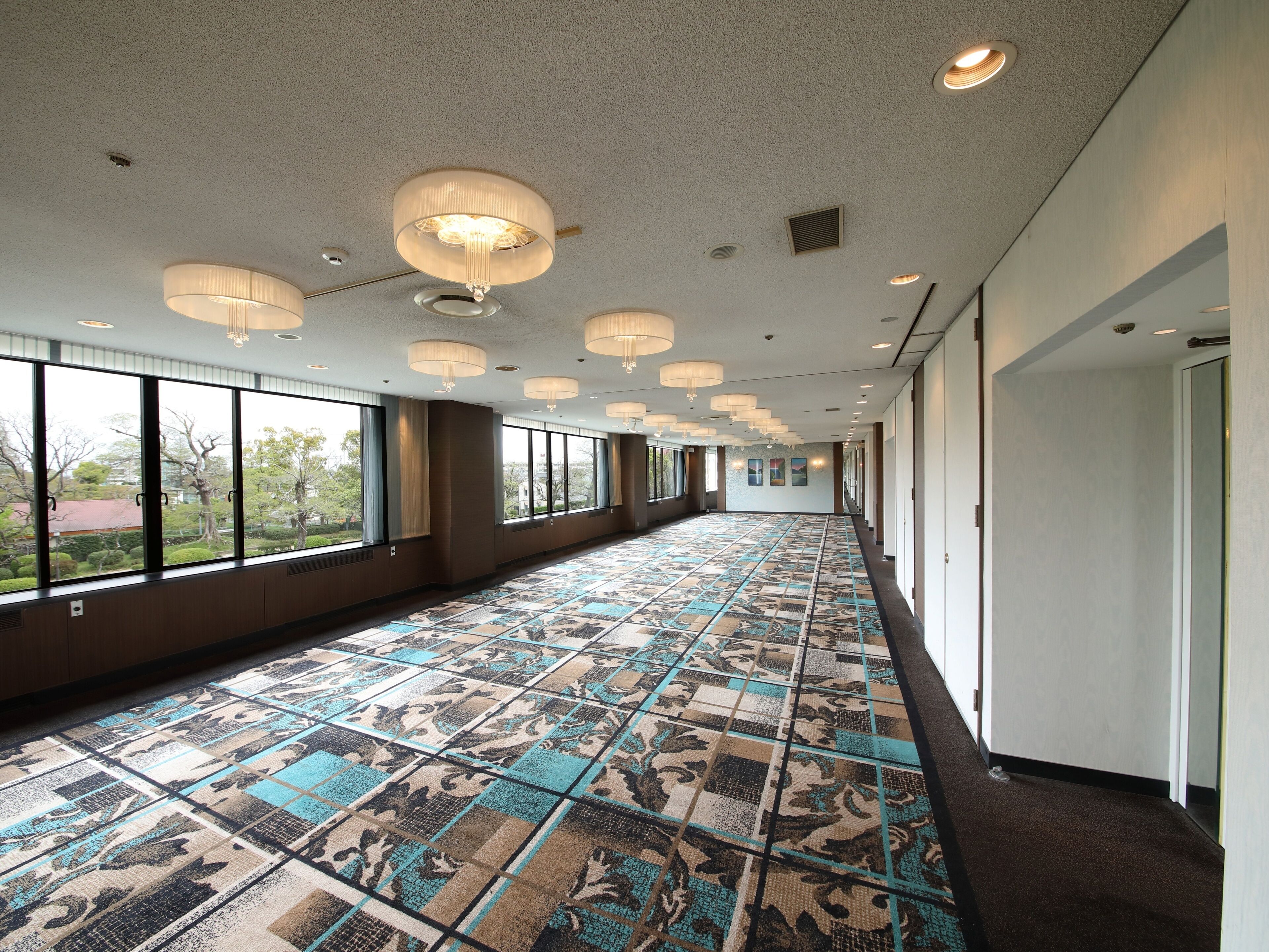 Un largo pasillo con alfombra estampada, ventanas grandes e iluminación empotrada.